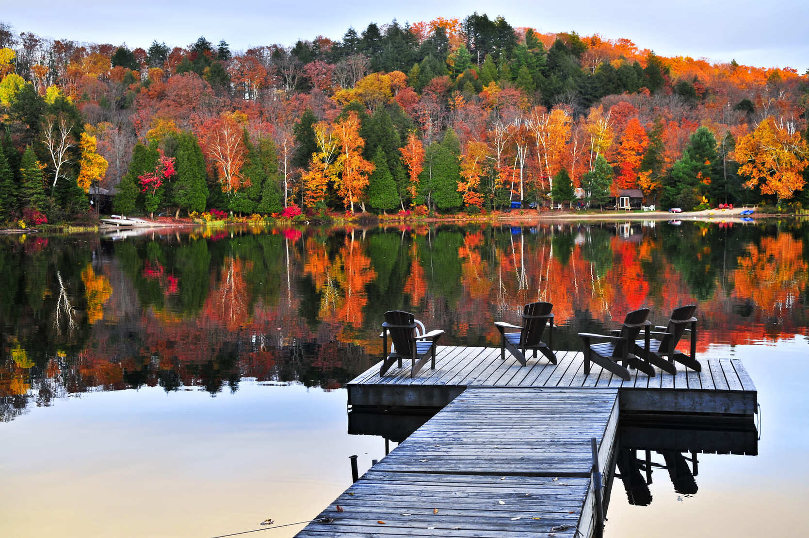 A dock with chairs sitting on a Central Ontario lake in the fall.